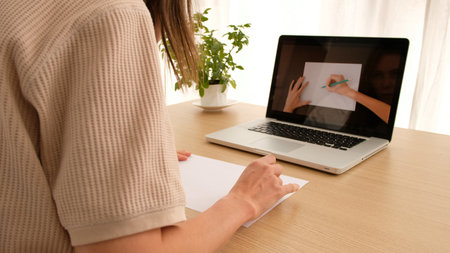 Woman learning to draw on an online course online sitting at home looking over her shoulder. Drawing...