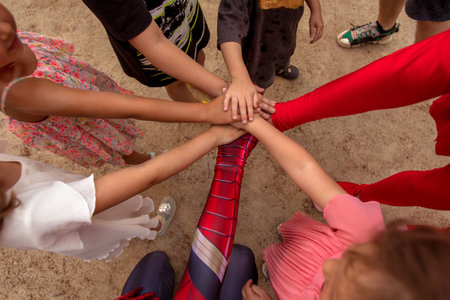 Top view of group of children stacking hands with animators in costumes during birthday party on...