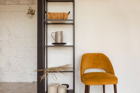 Comfortable chair placed near shelves with various accessories in cozy room at homeの写真素材