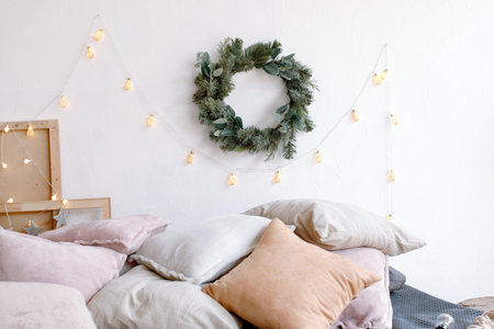 Cozy bed with pile of cushions in bedroom decorated with Christmas garland and wreath