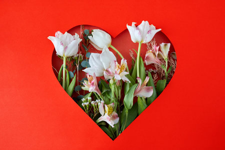 Hole in red paper in shape of heart through which tulips and leaves are visible. Happy valentines day conceptの写真素材