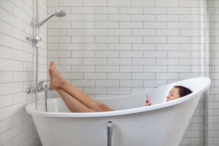 Woman using smartphone in white bathtub side viewの写真素材