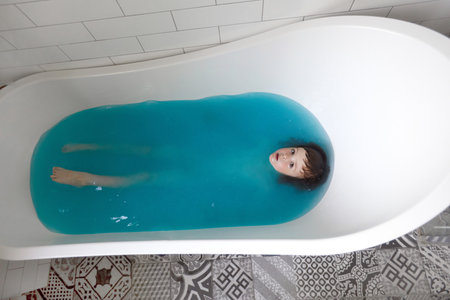 Cute child bathing in blue water in bathtubの写真素材