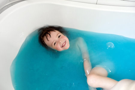 Cute child bathing in blue water in bathtubの写真素材