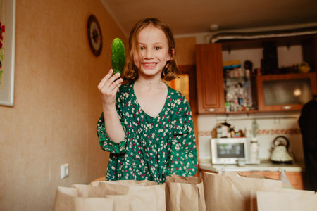 Happy girl showing cucumber in kitchenの写真素材