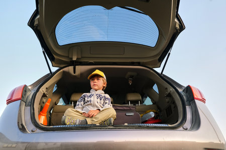 Kid sitting in open car trunk summer journeyの写真素材