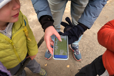 Faceless woman showing map on smartphone to anonymous childrenの写真素材