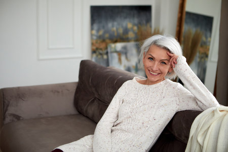 Stylish woman with gray hair on couchの写真素材