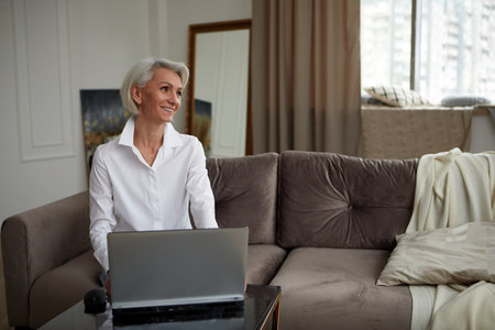 Adult cheerful woman working on laptop at homeの写真素材