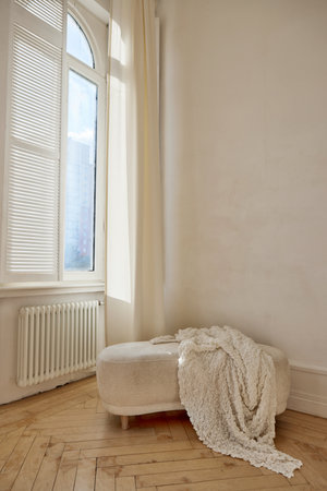Ottoman with blanket near window in light roomの写真素材