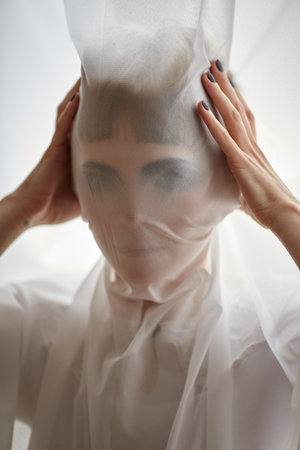 Woman portrait pulling fabric over her face hiding face maskの写真素材