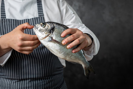 Crop male fishmonger holding raw fish black backgroundの写真素材