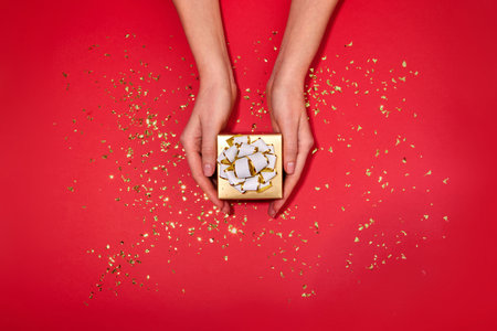 Female hands holding gift box red background. Christmas New Year Valentineの写真素材