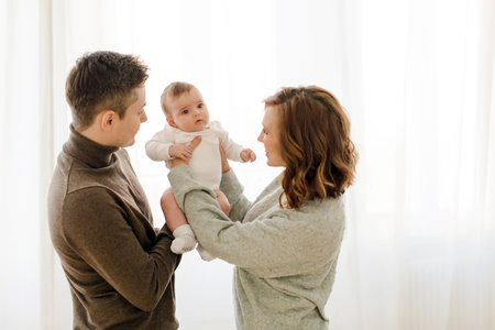 Happy couple carrying adorable baby near curtainの写真素材