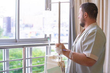 patient with a dropper looks out the window of the hospital room and smiles. back view. Healthcare concept.の写真素材