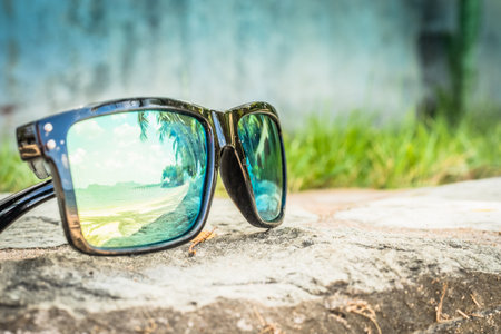 Fashionable sunglasses. Sunglasses with mirrored lenses. Reflection of the beach and tropical palm trees in sunglasses.の写真素材
