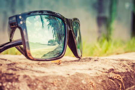 Fashionable sunglasses. Sunglasses with mirrored lenses. Reflection of the beach and tropical palm trees in sunglasses.の写真素材