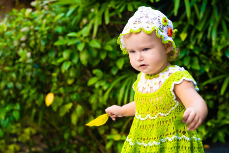 little girl in a knitted dress, chamomile, looks at the green leaves, the concept of children fashion. the child is surprisedの写真素材