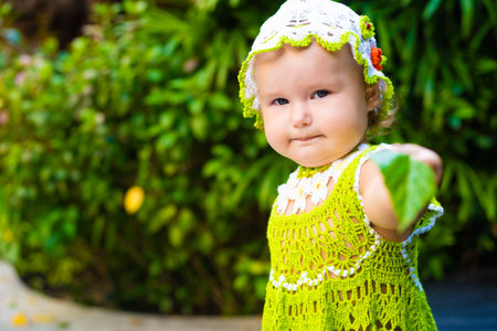 little girl in a knitted dress, chamomile, looks at the green leaves, the concept of children fashion. the child is surprisedの写真素材