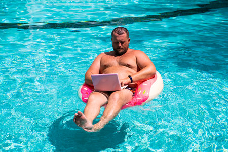 Dream job, a young man with a computer in the water on an inflatable circle,Man with a laptop on inflatable ring in the waterの写真素材