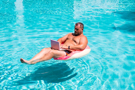 Male businessman with a laptop on rubber ring in the waterの写真素材