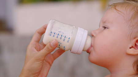 Cute girl drinking milk from a bottle in the gardenの写真素材