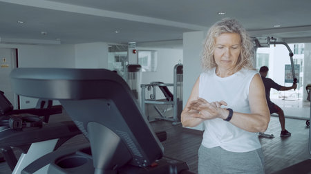 senior woman is engaged on a treadmill in the gym with a sports cardio clockの写真素材