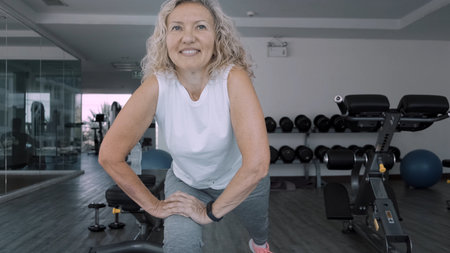Elderly woman makes squattings in the gym. Elderly woman Senior woman makes a sport exercises in the gymの写真素材
