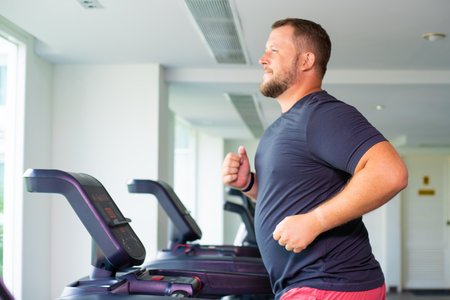 chubby man walking on running track, warming up on gym treadmill.の写真素材