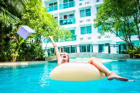 woman swims in the swimming pool in the pool and throws the laptop into the water. The girl is resting on the sea on an inflatable ring with a minicomputer. selective focusの写真素材