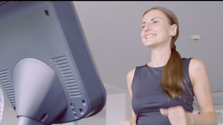 Beautiful fitness girl running and drinking water on treadmill at the gymの写真素材