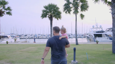 Pattaya, Thailand - May 10, 2019: Dad with a little daughter in his arms go to the marina of the yacht parking, slow motion, 4k.の写真素材