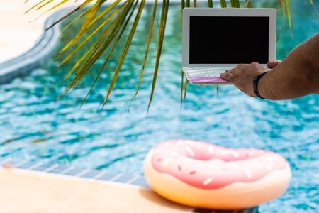 A man is typing on his laptop while sitting by the pool. Mens hands on the keyboard in the poolの写真素材