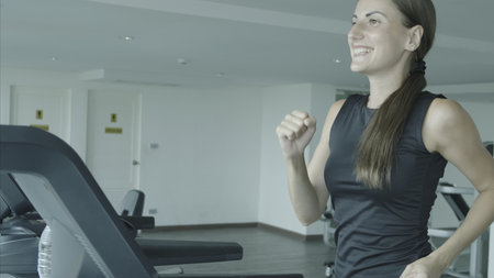 Beautiful fitness girl running and drinking water on treadmill at the gym