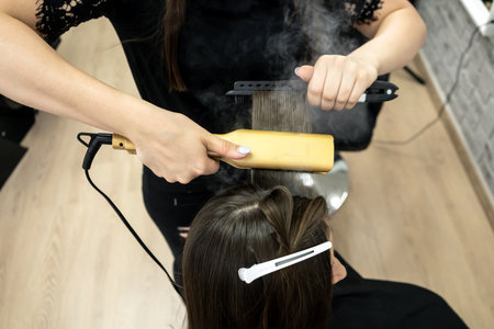 hairdresser makes hair lamination in a beauty salon for a girl with brunette hairの写真素材
