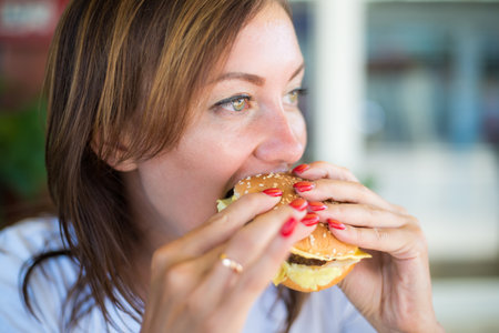 Young attractive girl, with an independent look, drinks beer and eats a burger. Close up. The concept of feminism and womens independence.の写真素材