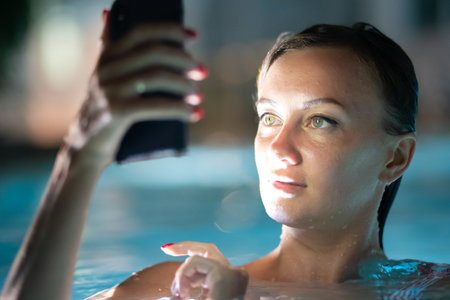 The girl in the pool, at night with the phone, the concept of vacation from businessの写真素材