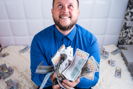 A nice man with a beard in a blue shirt, rejoices at the dollars, throws them up and counts. Win lotteryの写真素材