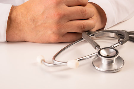 A doctor in white clothes is standing with his hands folded across his chest, a stethoscope hanging on his neck. Close upの写真素材