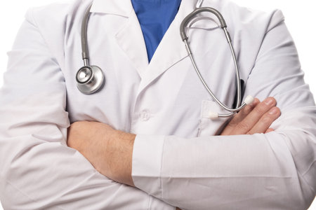 A doctor in white clothes is standing with his hands folded across his chest, a stethoscope hanging on his neck. Close upの写真素材