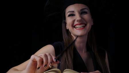 Attractive female witch with bright red lips with an open book of spells, smiles, conjures with the help of mechanical spiders and cobwebs.の写真素材