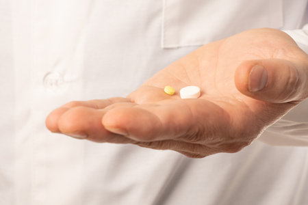The doctor in white clothes, and blue gloves, with a stethoscope on his neck, holds out pills. Close upの写真素材