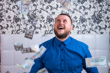 A nice man with a beard in a blue shirt, rejoices at the dollars, throws them up and counts. Win lotteryの写真素材