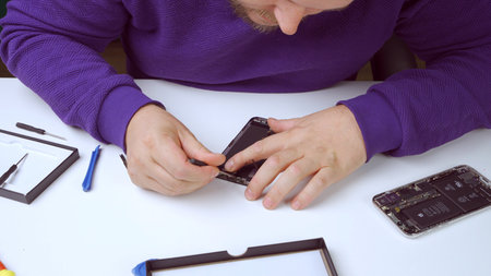 The smartphone repairman repairs the phone, using a screwdriver, unscrews the bolt to replace the smartphone screen. Close upの写真素材