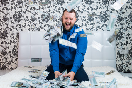 A nice man with a beard in a blue shirt, rejoices at the dollars, throws them up and counts. Win lotteryの写真素材