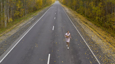 A female walks and runs along an asphalt road through an autumn forest, top view.の写真素材