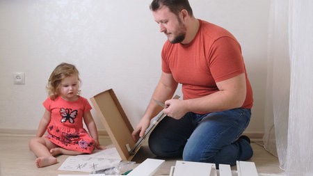 Dad and daughter collect furniture from chipboard. Dad and girl collect home furniture together.の写真素材