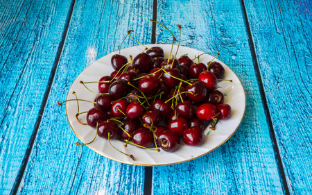 Sweet cherries on a white plate on a blue wooden table