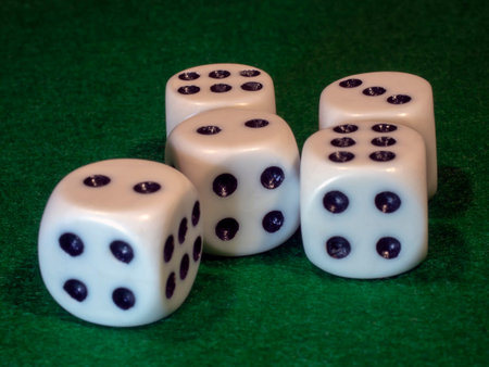 The bone cube of white color with black points for gamblings lies on green cloth.