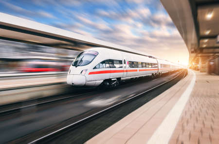 White modern high speed train in motion on railway station at sunset. Train on railroad track with...